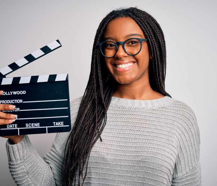 Young african american director girl filming a movie using clapboard over isolated background with a happy face standing and smiling with a confident smile showing teeth