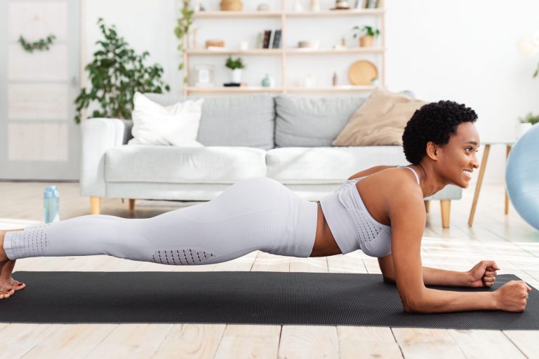 Home workout. Black woman training on yoga mat, doing elbow plank pose, strengthening her abs muscles. Side view of fit millennial lady exercising indoors, leading active lifestyle